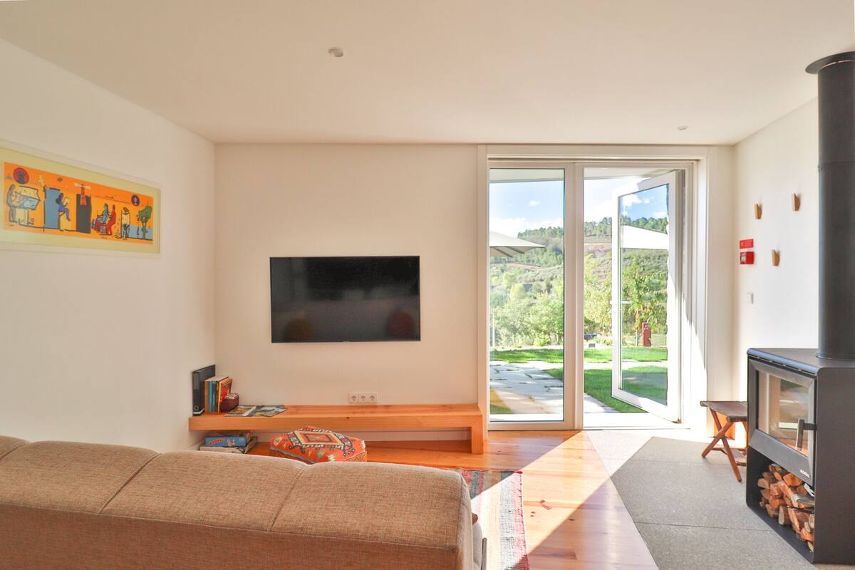 A modern living room with a flat-screen TV, a sofa, a wooden bench, and a fireplace.