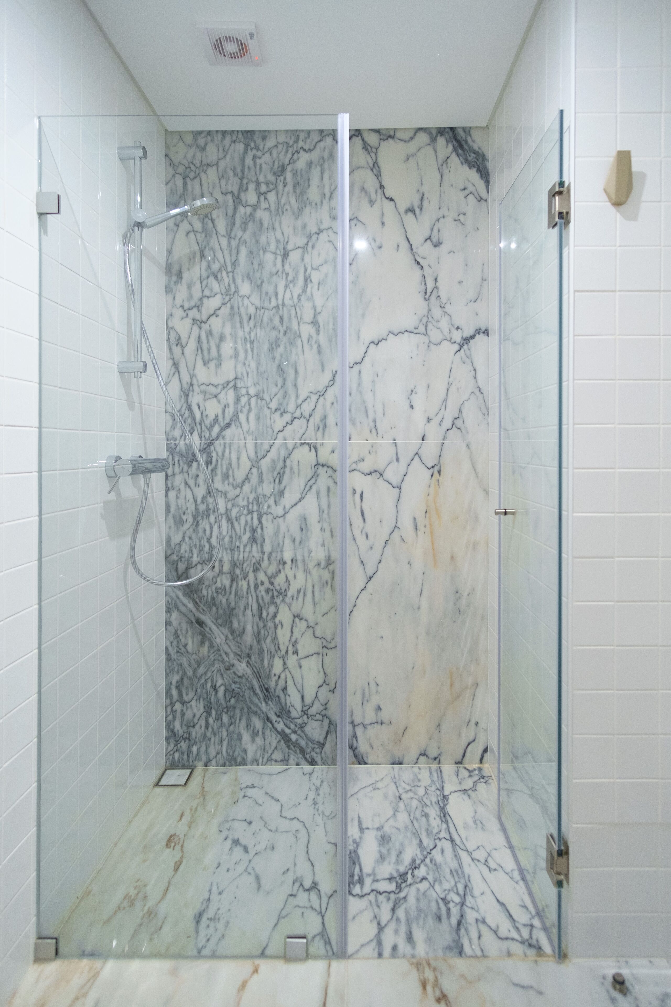 A glass-enclosed shower with marble walls and floor.