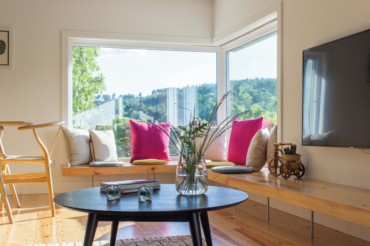 A modern living room with a large window, a round table, and a flat-screen TV.