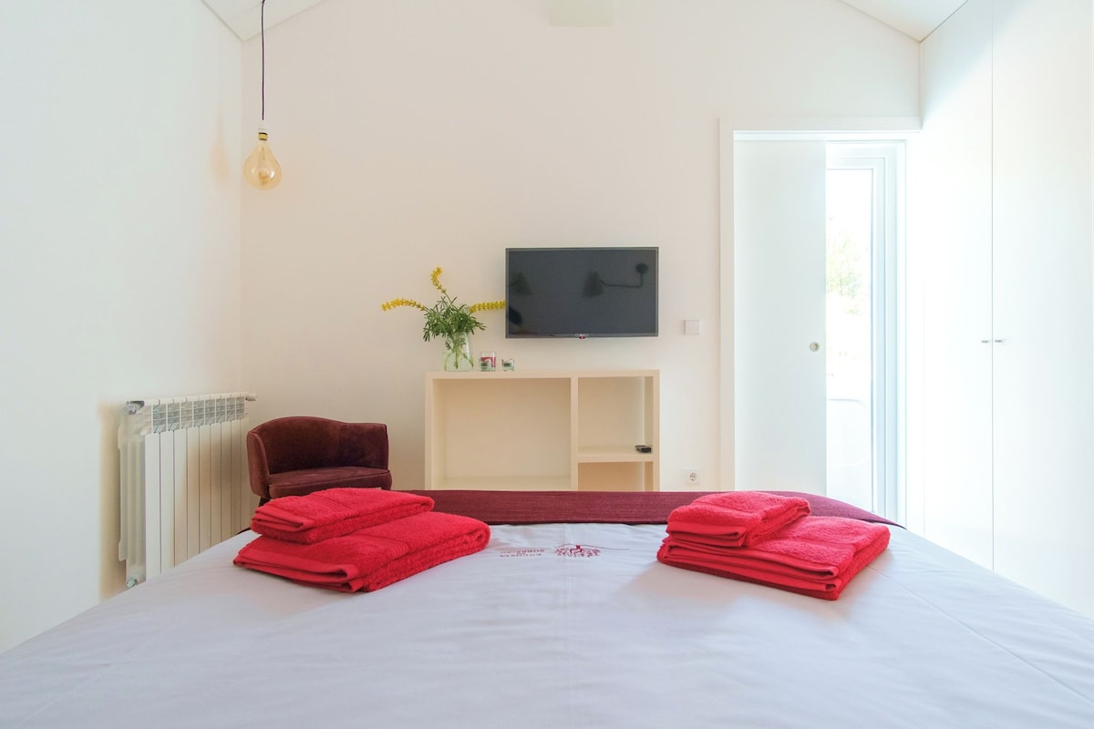 Quarto de hotel com cama, uma cadeira, televisão e radiador.
