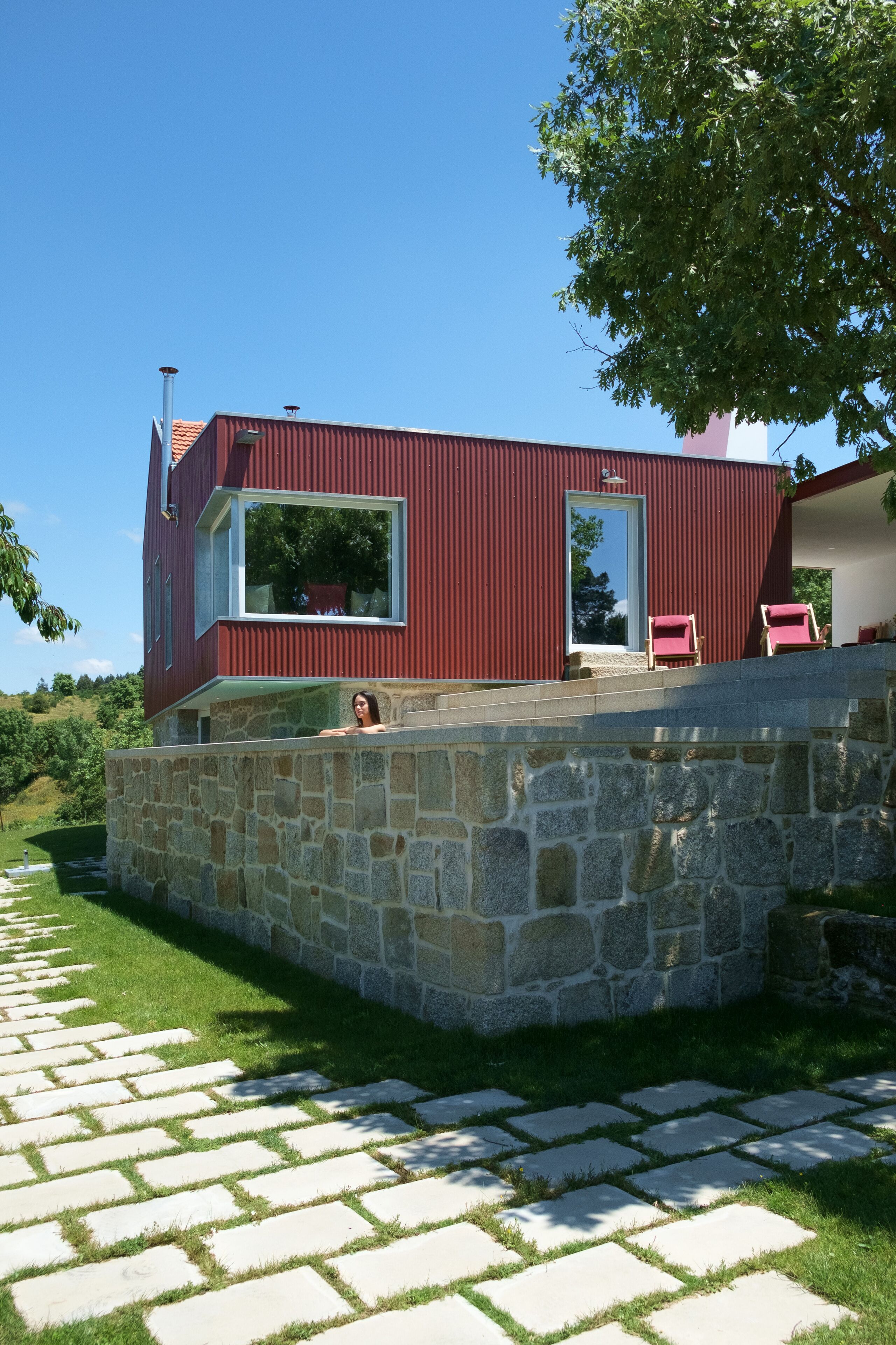 Um edifício moderno vermelho com uma parede de pedra e um caminho pavimentado que o leva até ele.