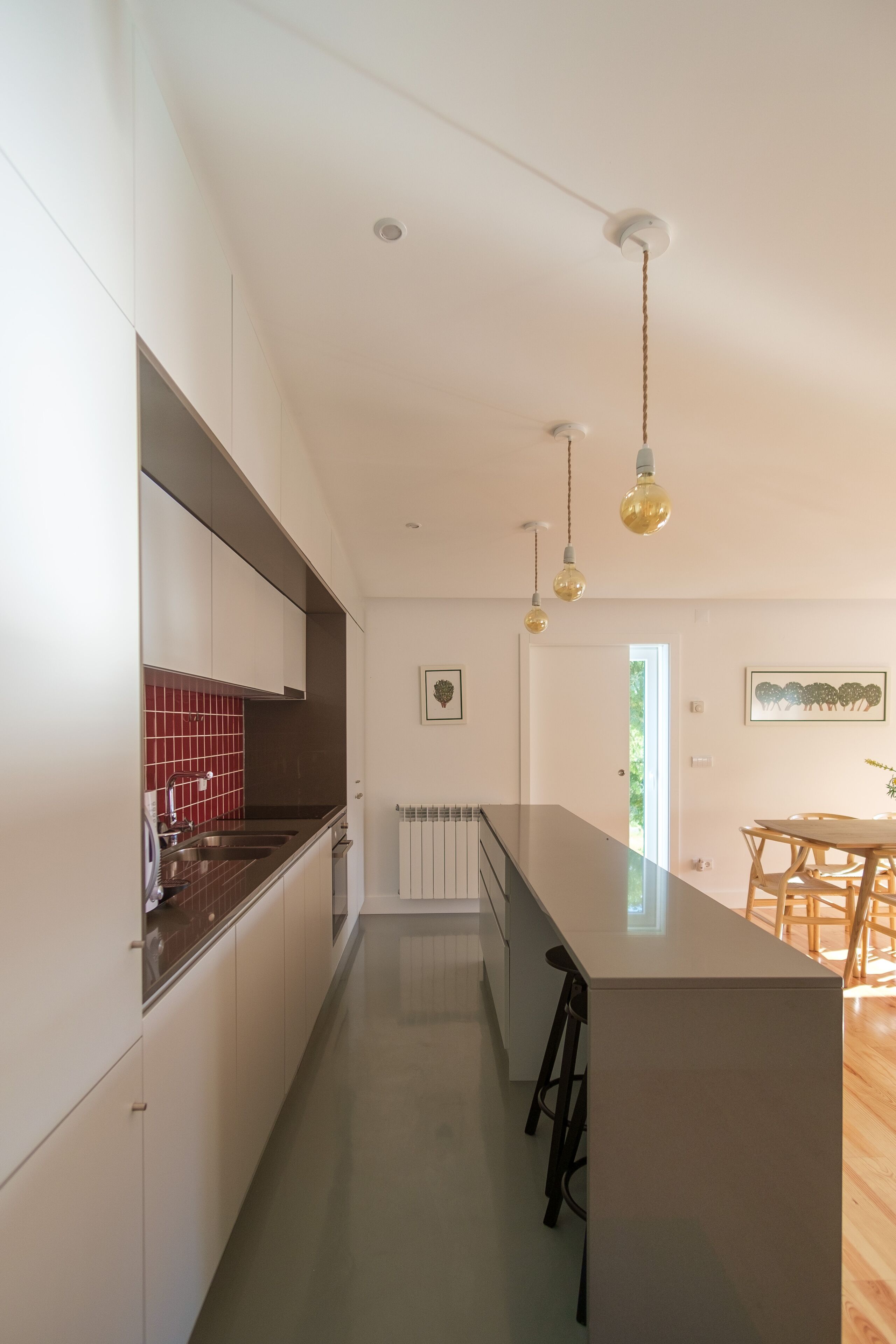 Una cocina moderna con armarios blancos, salpicadero rojo e iluminación colgante.
