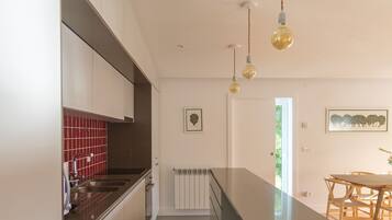 Una cocina moderna con armarios blancos, salpicadero rojo e iluminación colgante.