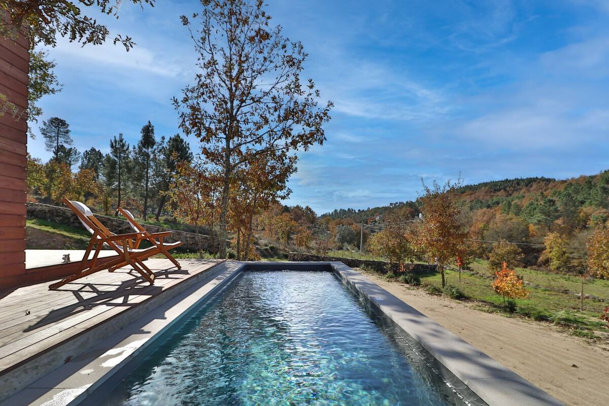 A rectangular pool with clear water, surrounded by a wooden deck and lounge chairs.