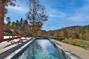 A rectangular pool with clear water, surrounded by a wooden deck and lounge chairs. - Encosta do Sobreiro - Serra da Estrela (Fornos de Algodres)