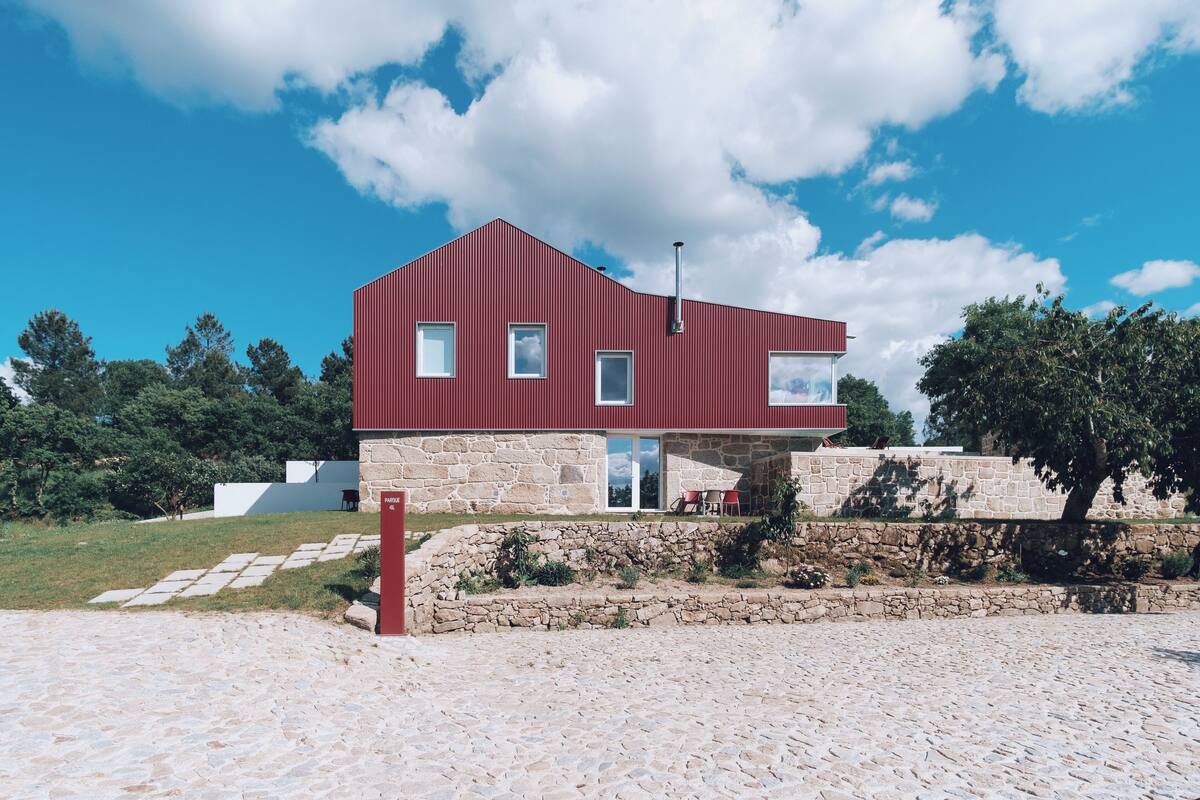 A modern red building with stone walls, large windows, and a stone pathway leading to it.