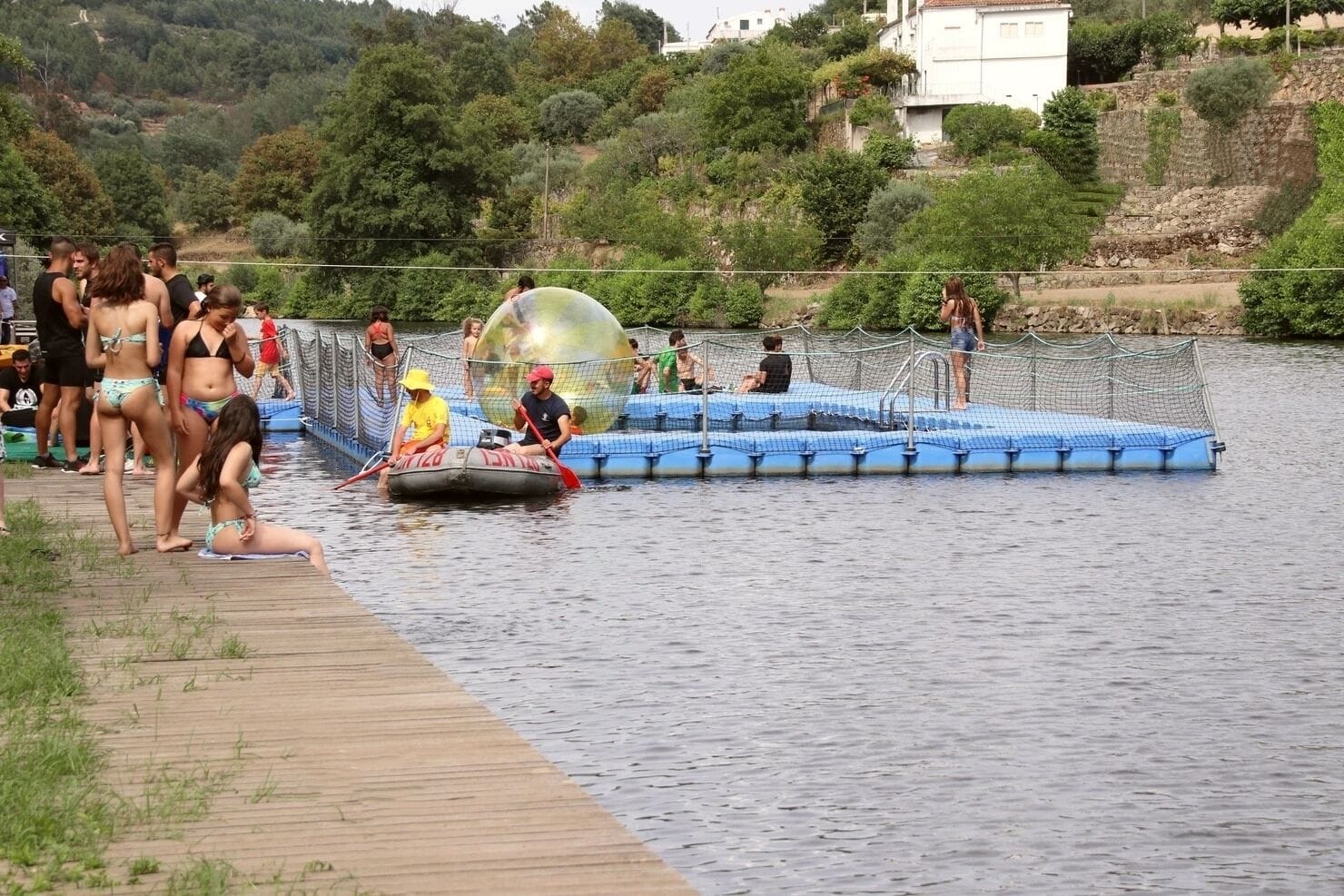 A water activity area with a wooden deck and a floating platform with people engaging in water sports.