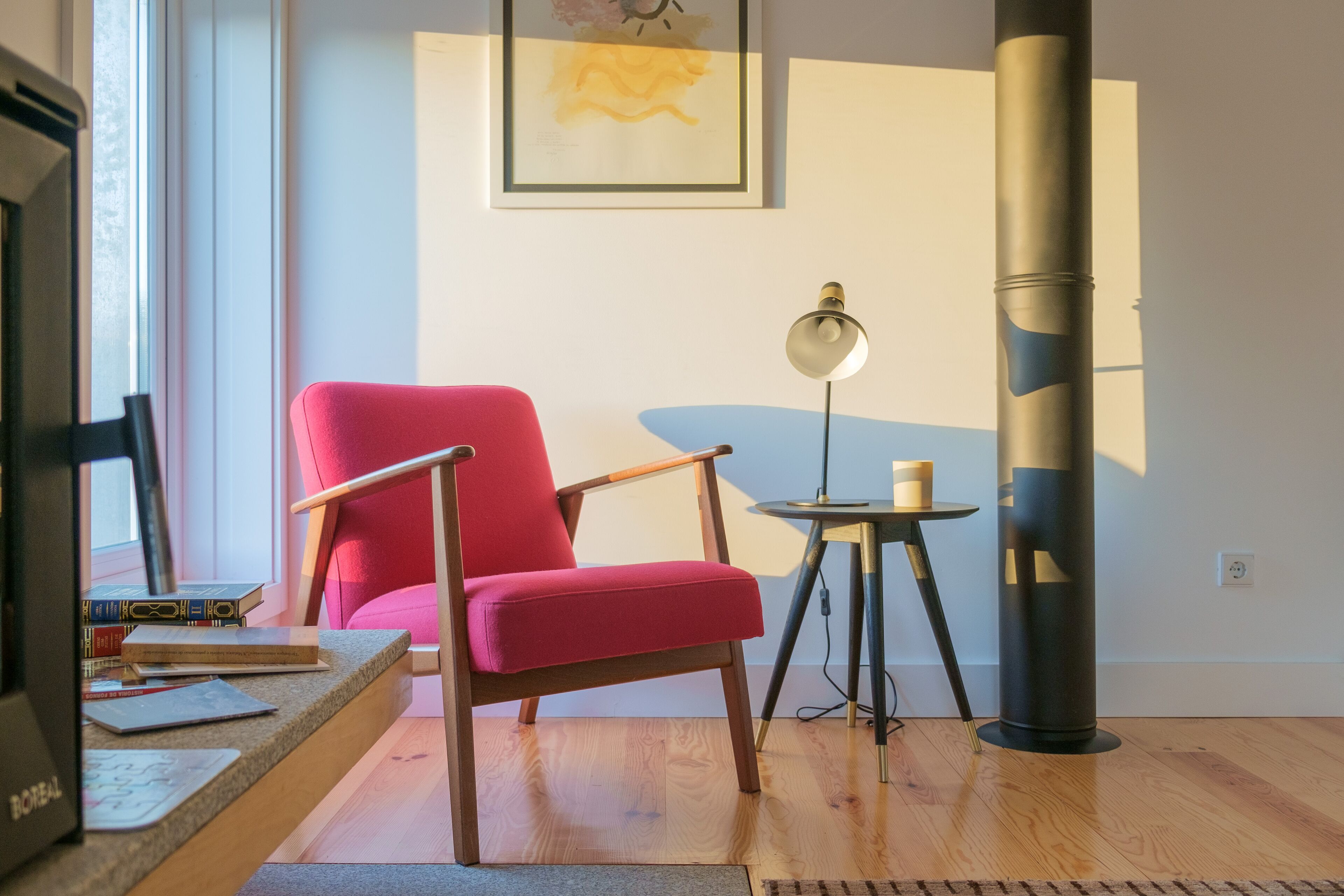 Un salón moderno con una silla roja, una mesita redonda con una lámpara y una estantería.
