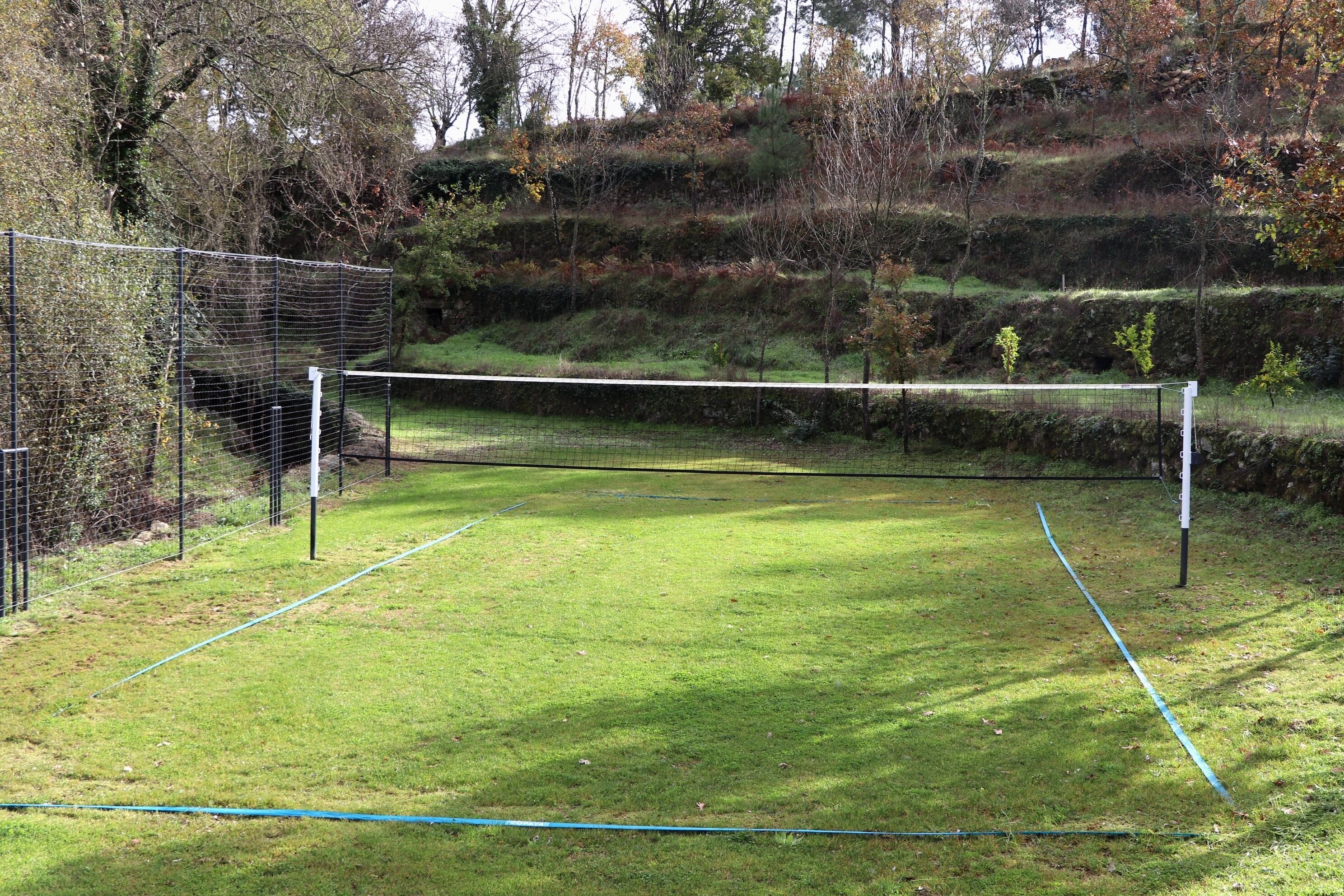 Een tennisbaan met een net, omringd door een gaashek en bomen.
