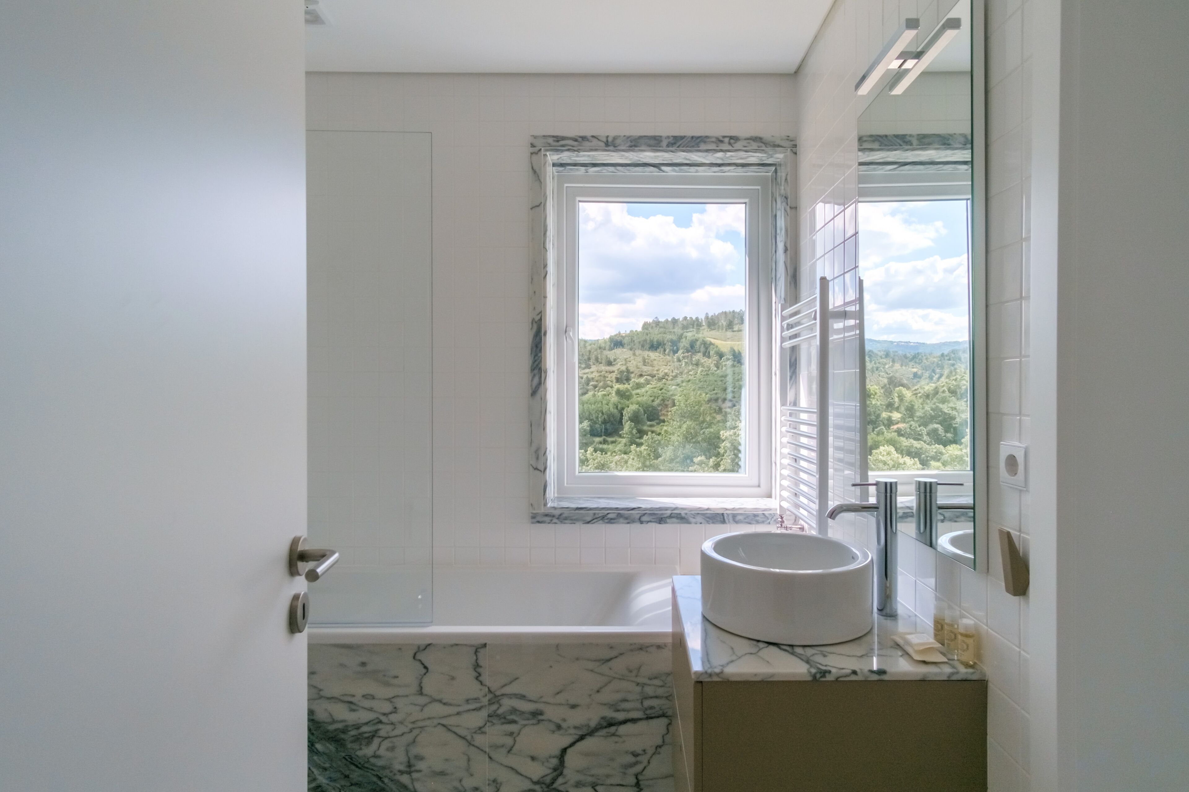 Une salle de bain équipée d’une baignoire, d’un lavabo et d’une fenêtre donnant sur un paysage verdoyant.