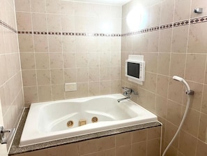 Un baño con bañera, cabezal de ducha manual y panel de control en la pared.