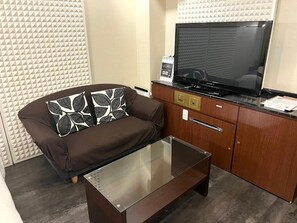 Una sala moderna con un sofá, una mesa de centro de vidrio, un mueble de madera y un televisor de pantalla plana.