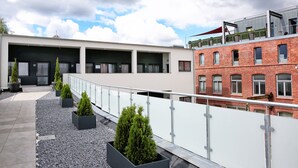 Terraço no telhado com um edifício moderno, plantas em vasos e céu claro.