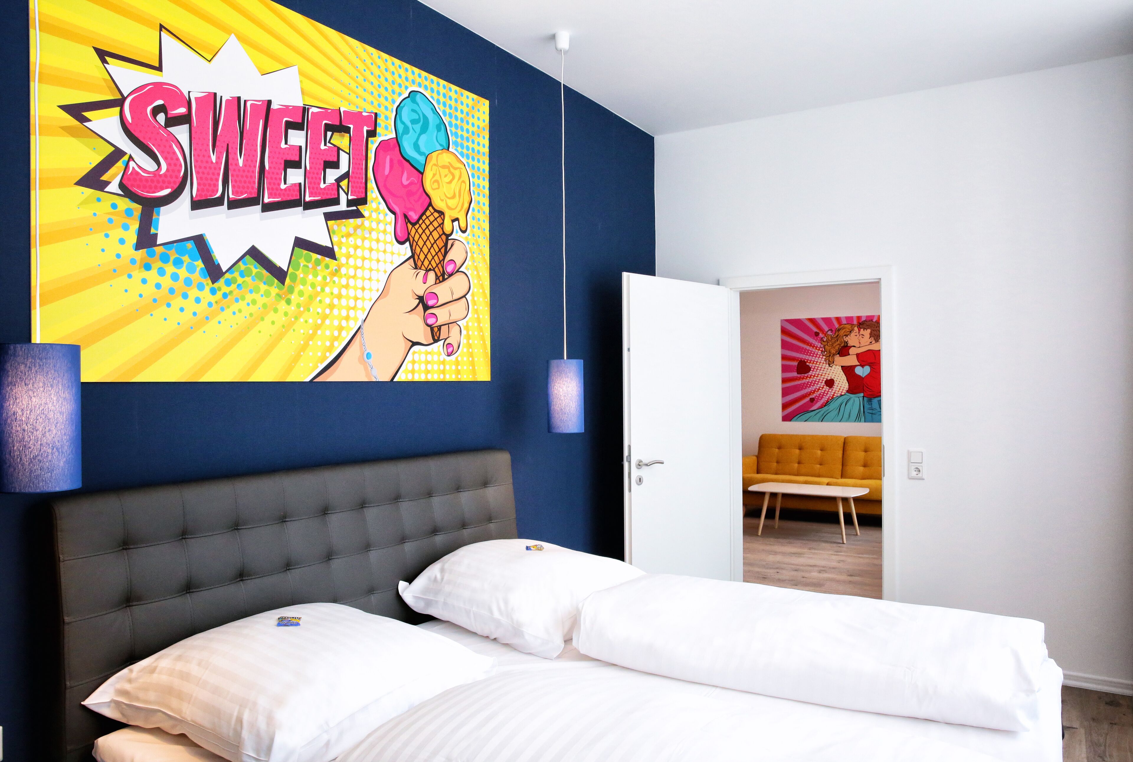 Una habitación de hotel moderna con una cama grande, un cabecero y un mural llamativo en la pared.