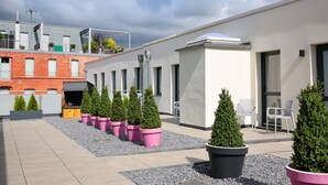 Terraço no telhado com árvores em vasos, um edifício de tijolos e um edifício branco moderno.