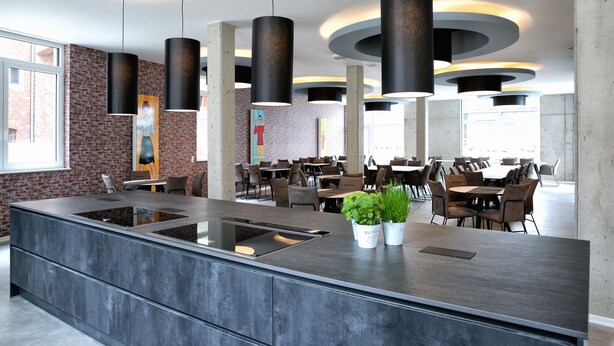Um restaurante moderno com ilha central, luminárias pendentes pretas e paredes de tijolo.