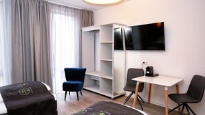 Quarto de hotel com cama, escrivaninha, cadeira, guarda-roupa e televisão.