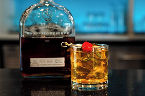 A bottle of Woodford Reserve whiskey and a glass with a strawberry garnish on a bar counter.