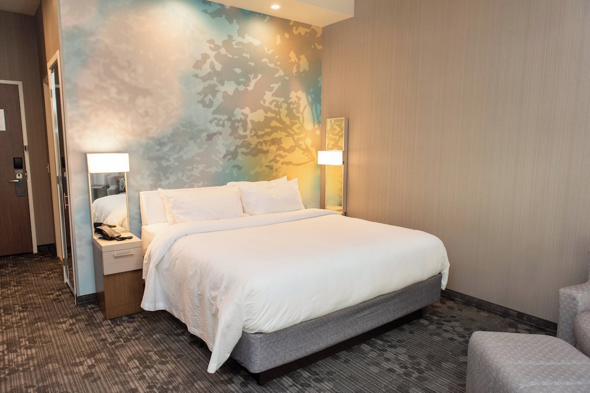 Ein Hotelzimmer mit einem großen Bett, zwei Nachttischen mit Lampen, einem Sessel und Teppichboden.