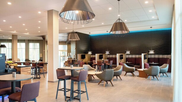 A modern restaurant with high ceilings, pendant lighting, and a mix of seating arrangements including bar stools and tables. - Courtyard by Marriott Mesa At Wrigleyville West (Mesa)