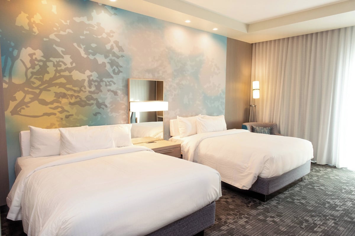 Ein Hotelzimmer mit zwei Betten, einem großen Spiegel, einem Nachttisch und einer Lampe.