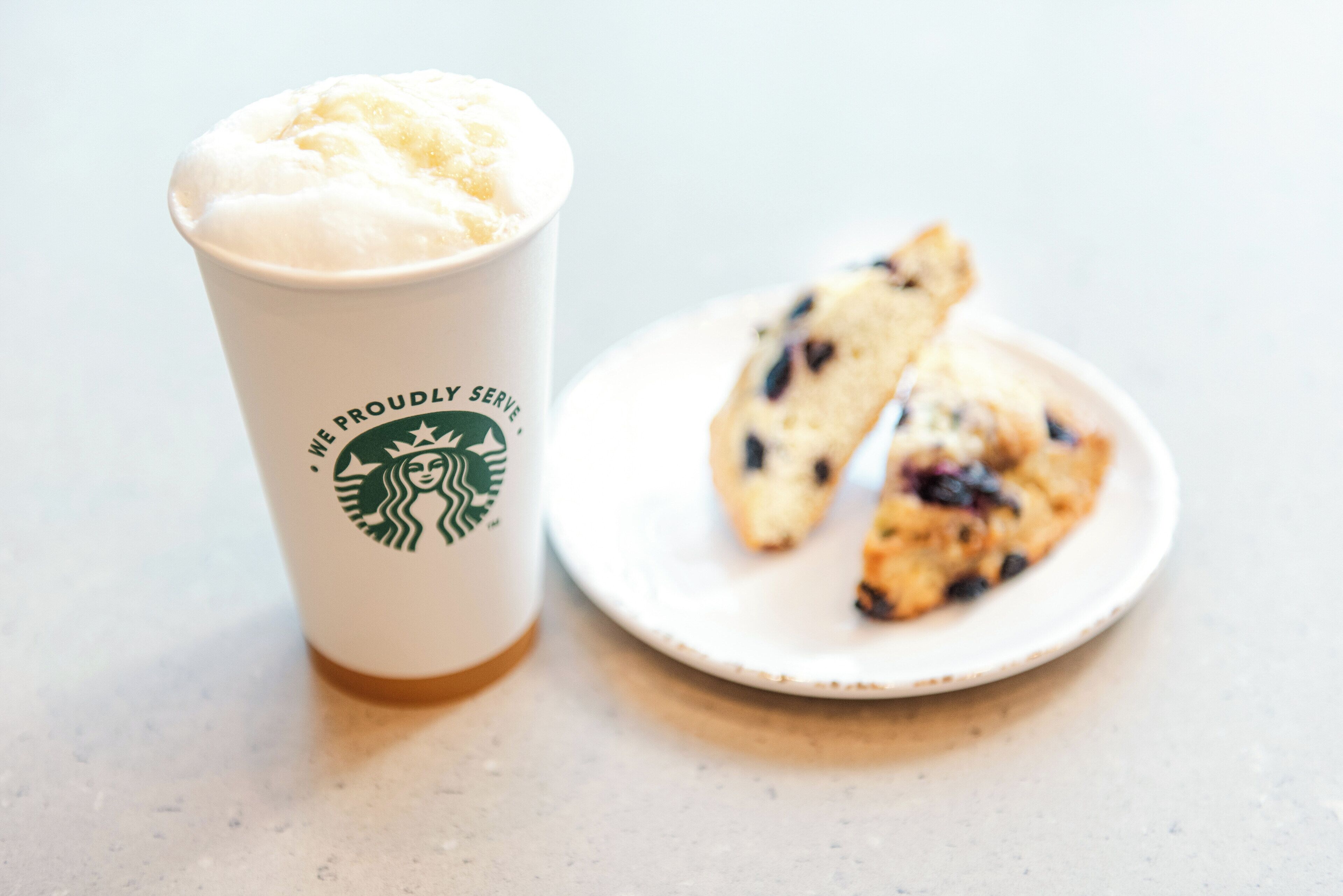 En Starbucks-mugg med en dryck toppad med skum och en tallrik med blåbärsmuffins.