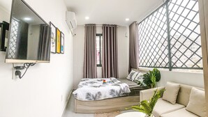 A modern bedroom with a bed, a sofa, a TV, and a window with a view.