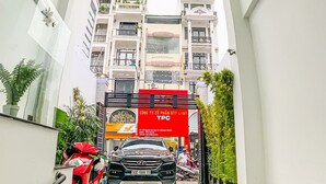A modern building entrance with a glass facade, a red banner, and a black car parked in front.