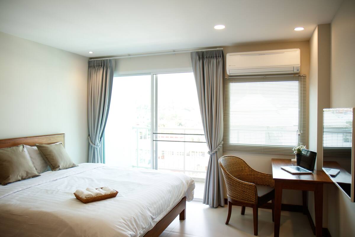 A hotel room with a bed, a desk with a laptop, and a window with curtains.
