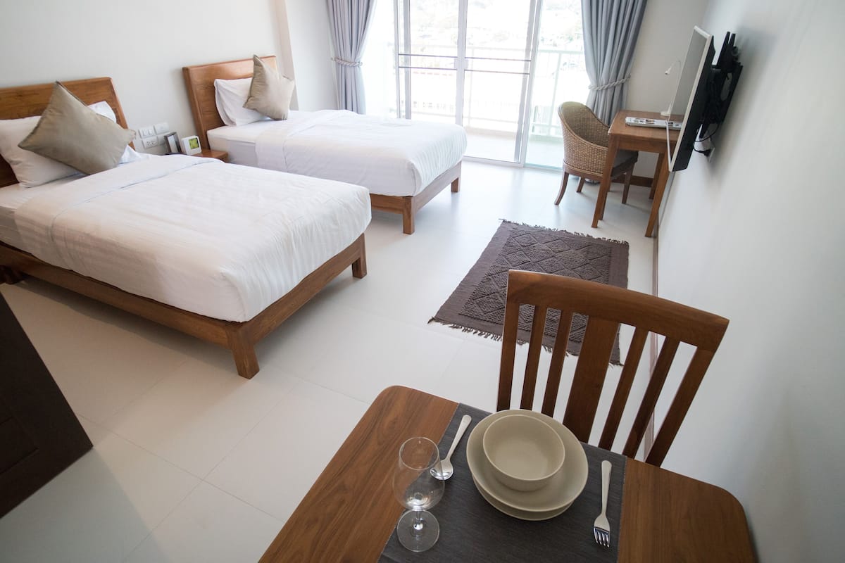 A hotel room with two beds, a dining table with cutlery, and a TV on a stand.