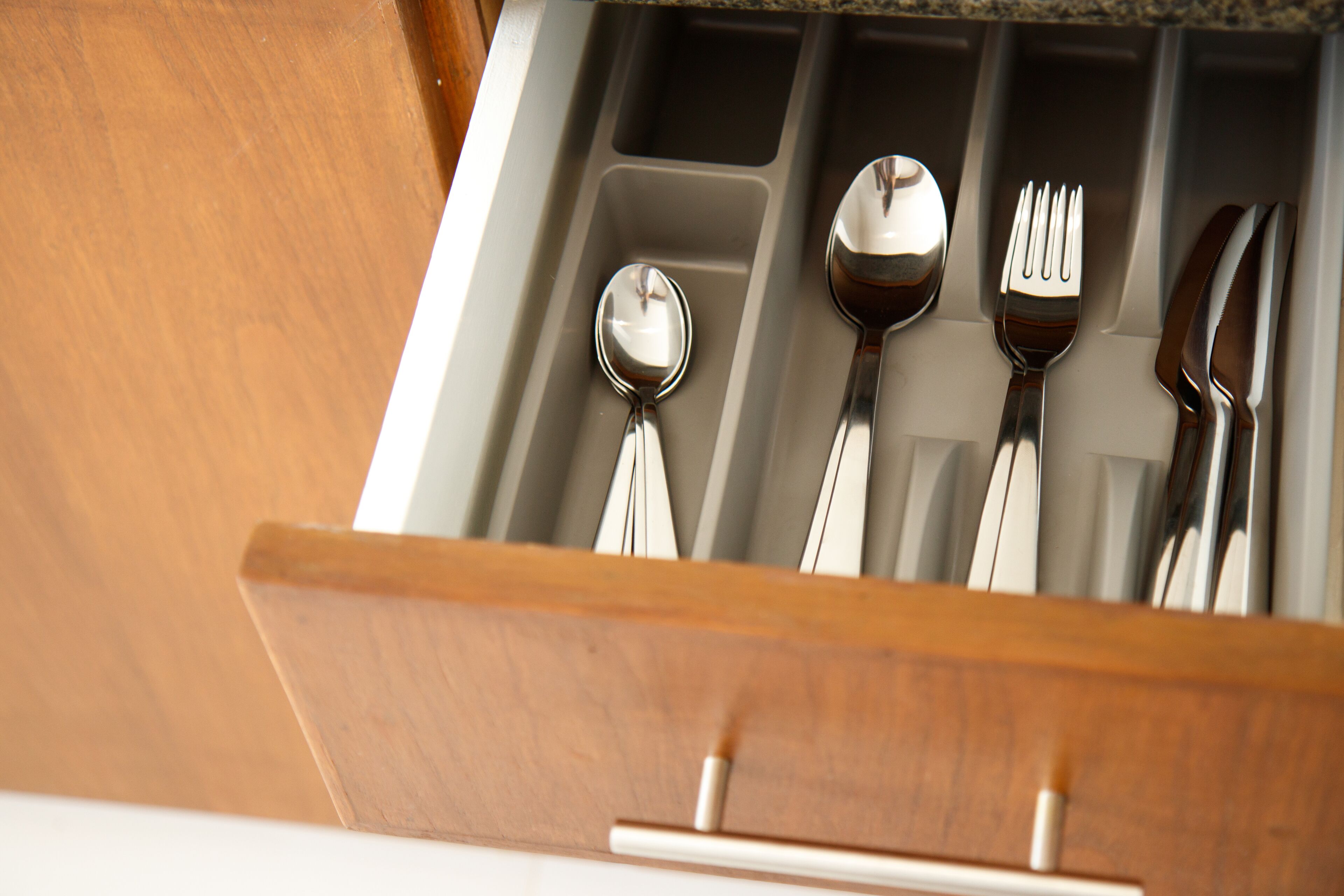 Un cajón con utensilios de cocina, como cuchara, tenedor y cuchillo.