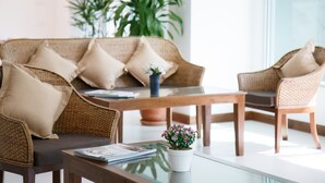 Ein modernes Wohnzimmer mit einem Rattan-Sofa, zwei Sesseln, einem Couchtisch und einer kleinen Topfpflanze.
