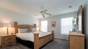 A bedroom with a wooden bed, nightstands, a dresser, a ceiling fan, and a large window with blinds. - Wooded View/Game Room/ Pool/Close to WDW (Davenport)