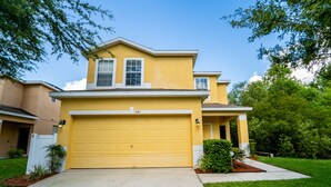 A yellow two-story house with a garage, a small porch, and a well-maintained lawn. - Wooded View/Game Room/ Pool/Close to WDW (Davenport)