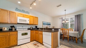 A kitchen with wooden cabinets, a microwave, an oven, and a dishwasher. There is a dining area with a table and chairs. - Wooded View/Game Room/ Pool/Close to WDW (Davenport)