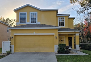 A two-story residential building with a yellow facade, a garage, and a front door with a mailbox and a street sign.