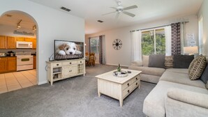 A living room with a TV, sofa, coffee table, and a kitchen area visible through an archway. - Wooded View/Game Room/ Pool/Close to WDW (Davenport)