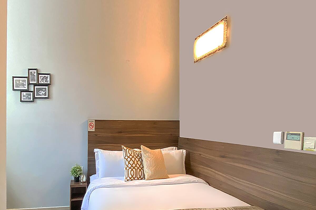 A hotel room with a wooden headboard, a bed with white linens, a patterned throw, a nightstand with a plant, and framed pictures on the wall.
