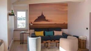 En moderne stue med et stort vægmaleri, en sofa med farverige puder, et sofabord og et sidebord.