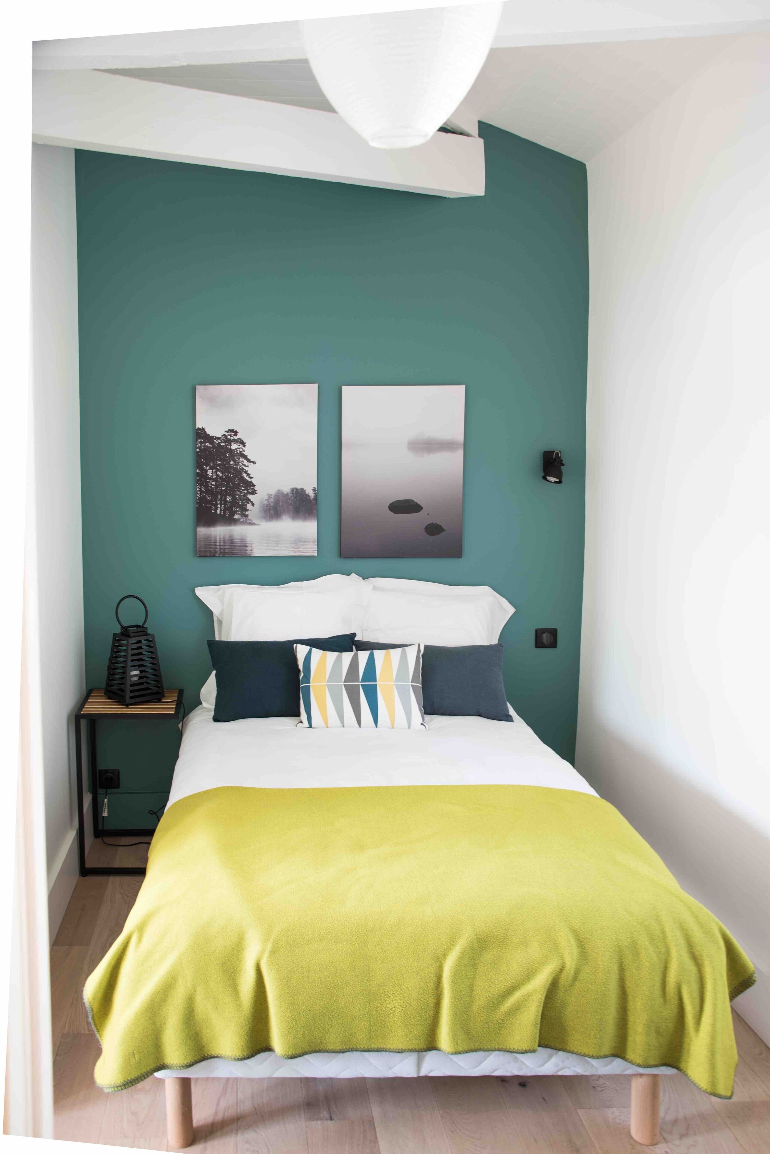 Un dormitorio con paredes color turquesa, una cama blanca y dos cuadros enmarcados.