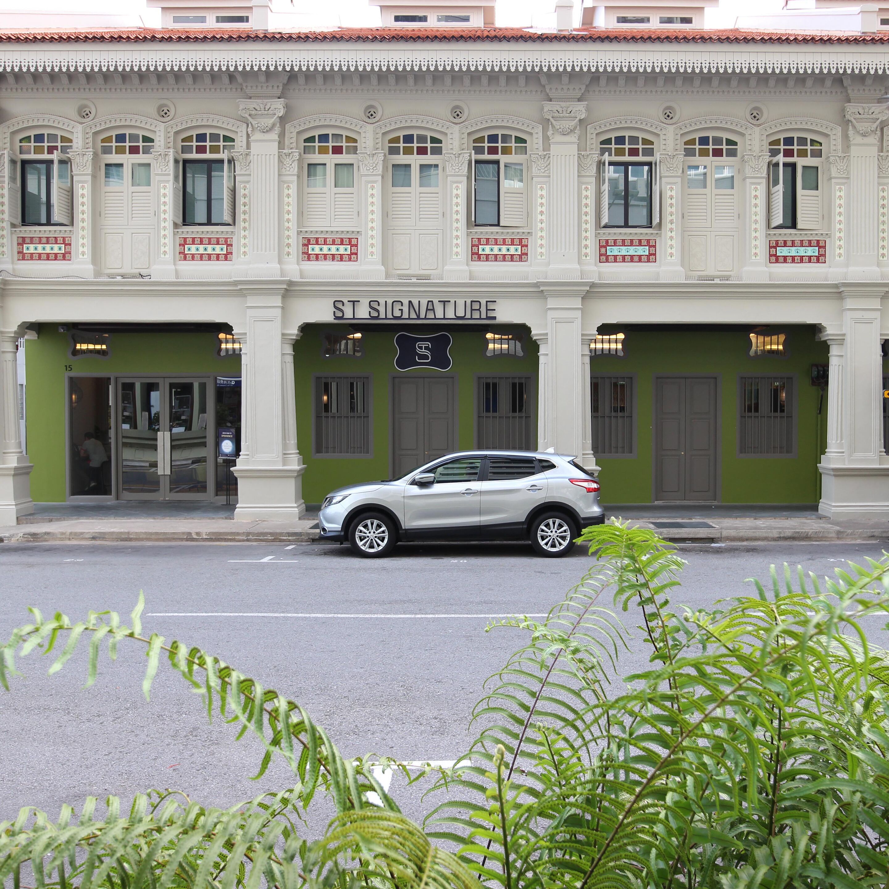 A building with a sign reading "ST SIGNATURE" and a silver car parked in front.