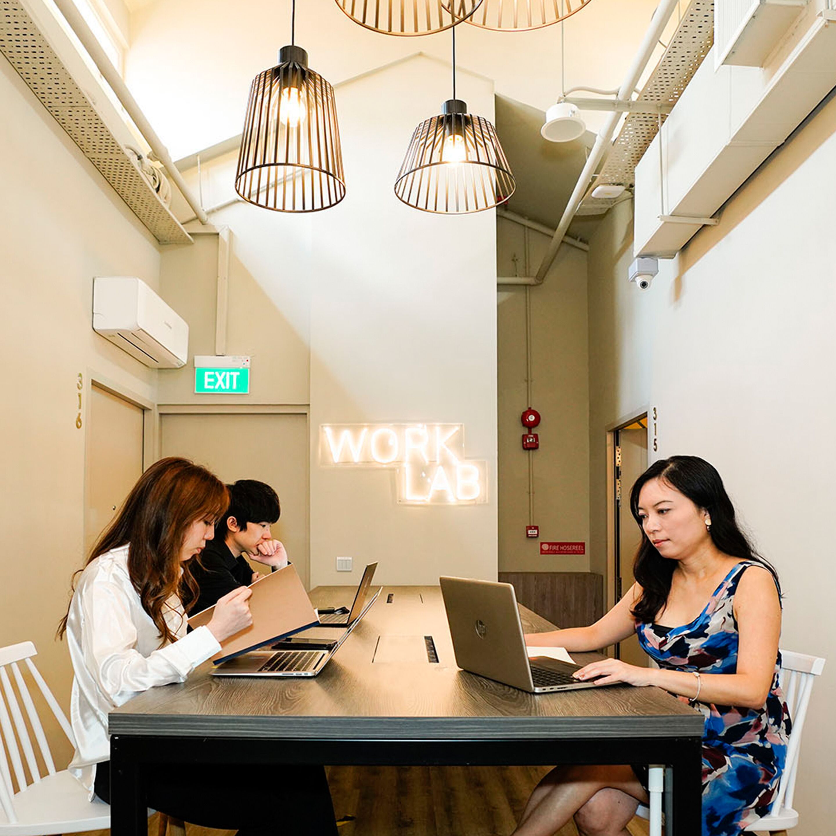 A modern workspace with three individuals working at a table, equipped with laptops.