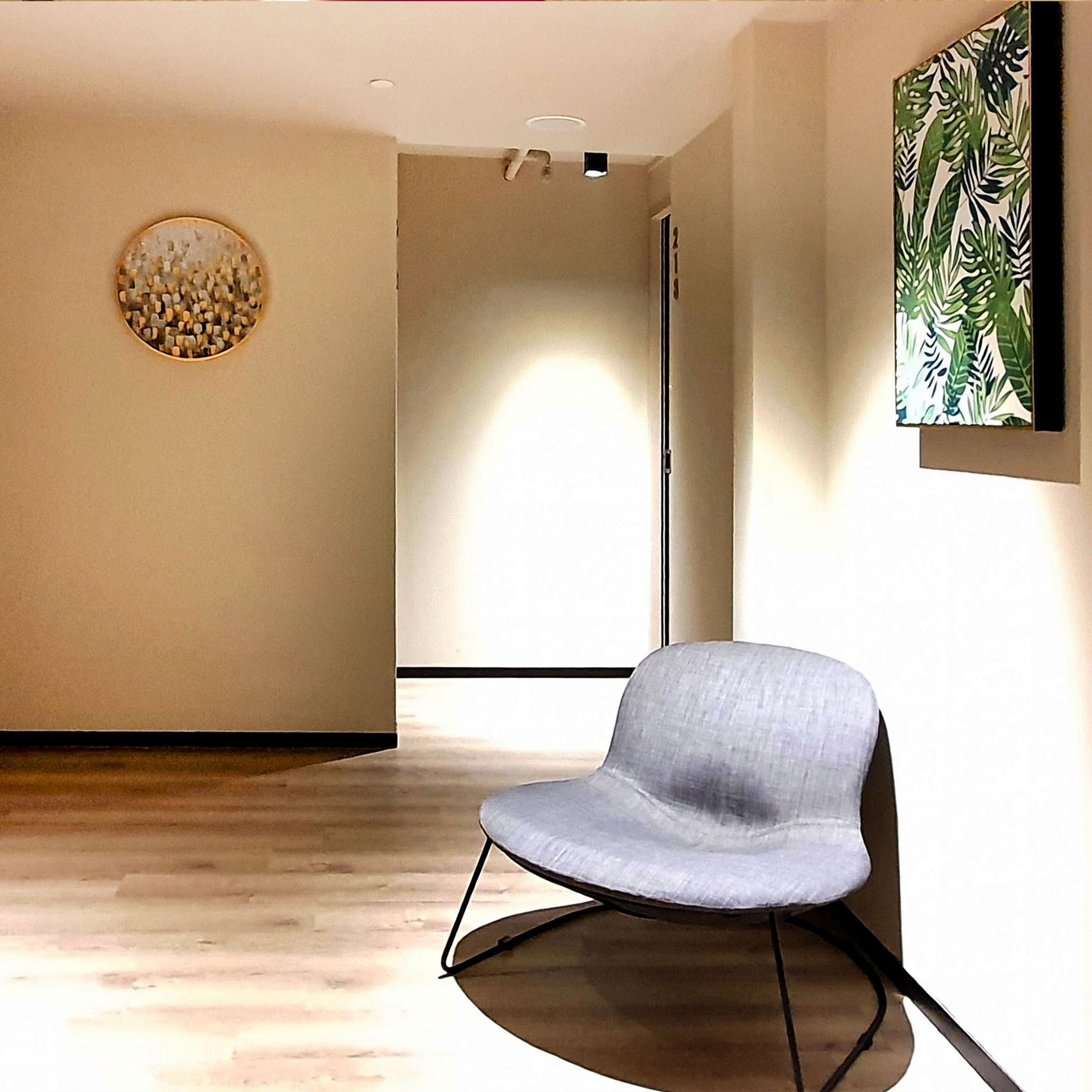 A modern interior with a grey upholstered chair, a round decorative wall piece, and a large abstract painting.