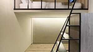 Ein modernes Schlafzimmer im Loft-Stil mit Hochbett, Treppe und einer kleinen Sitzecke mit Lampe.