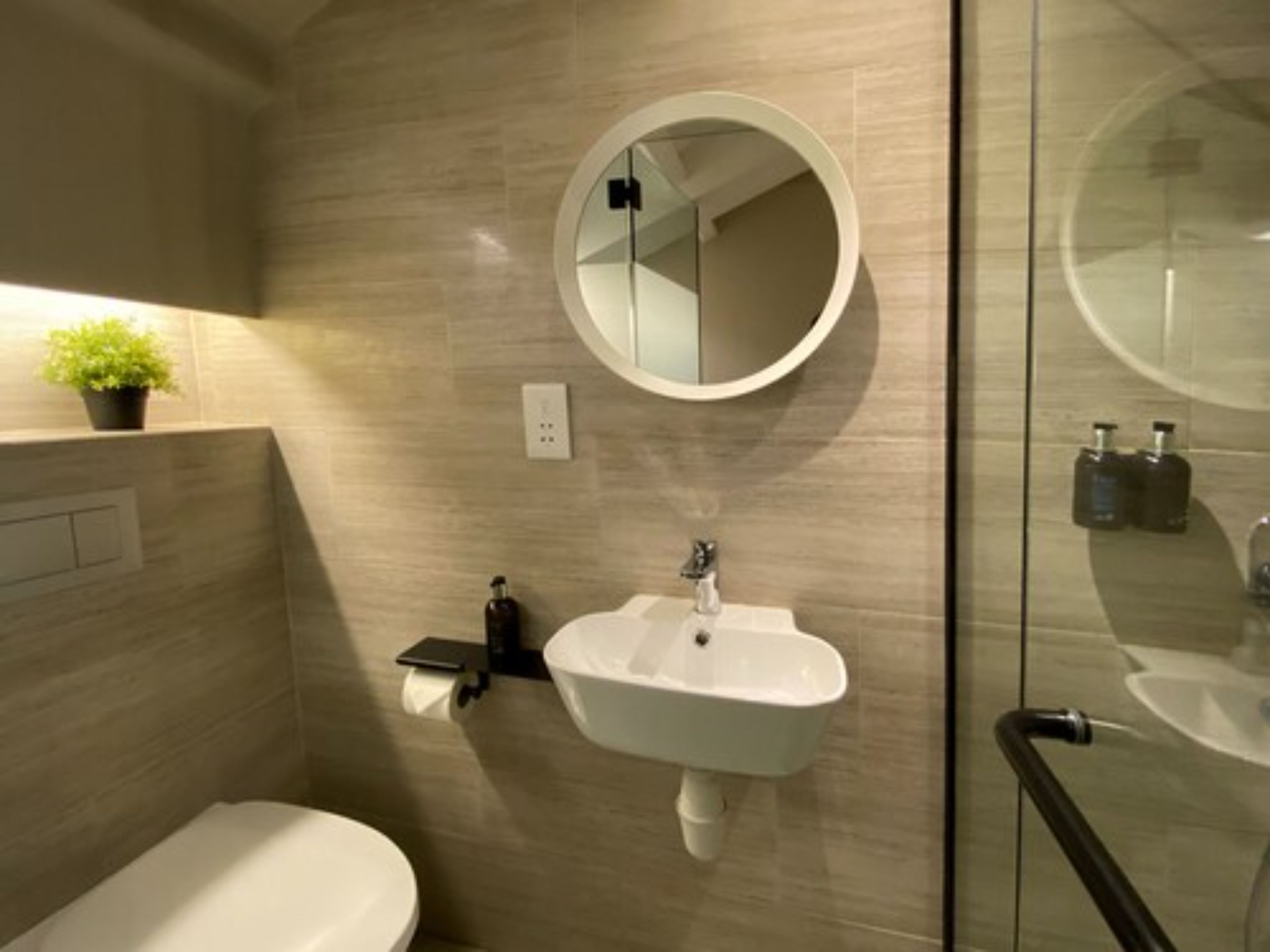 Un baño moderno con inodoro, lavamanos con espejo y cabina de ducha de vidrio.