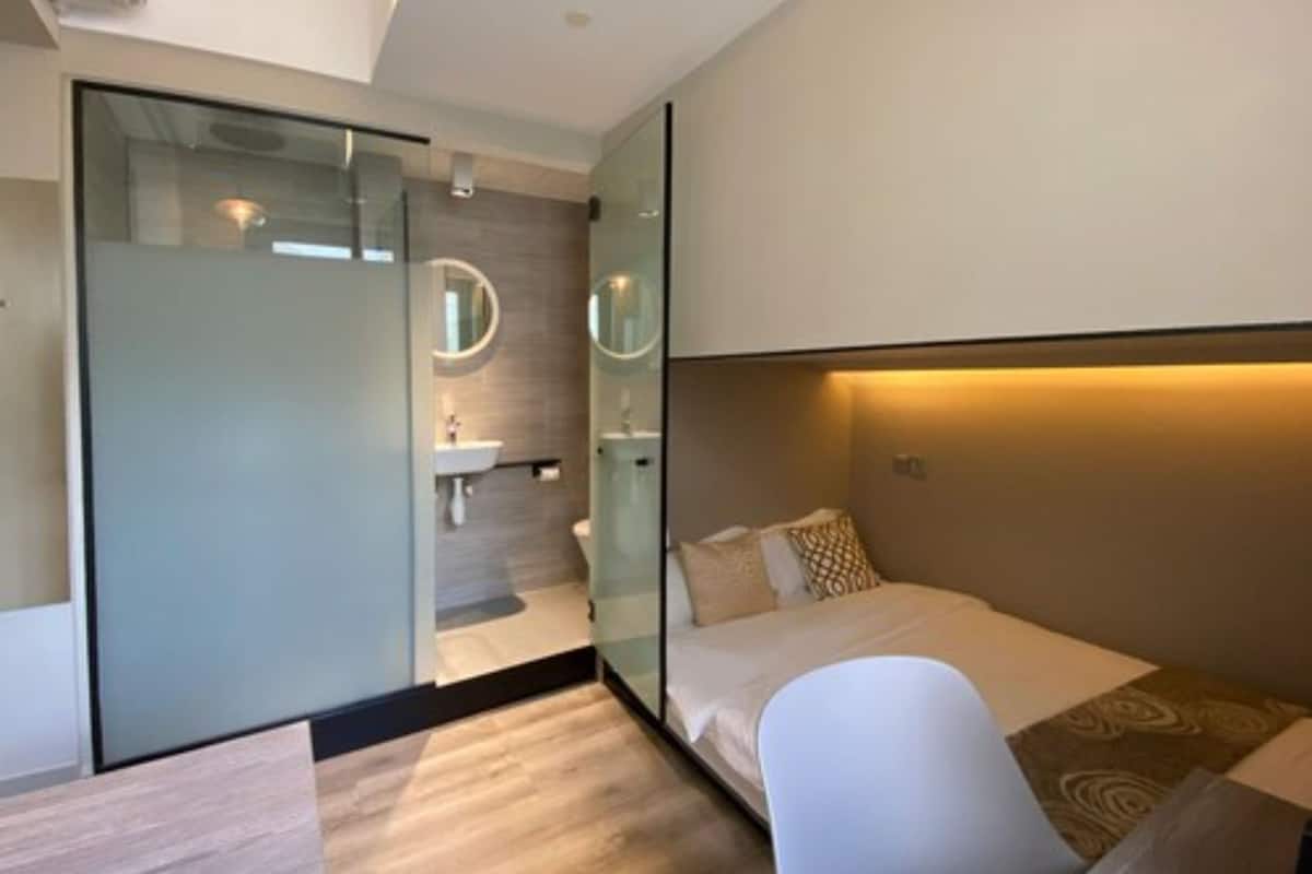 Quarto de hotel moderno com divisória de vidro separando o quarto do banheiro.