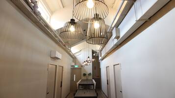 A narrow hallway with a wooden table and chairs, white walls, and hanging pendant lights.