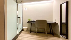 Habitació d'hotel amb llit, escriptori, cadira, paperera petita i mirall.