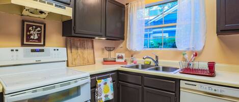 A kitchen with dark cabinets, a white stove, a sink, and a window with curtains.