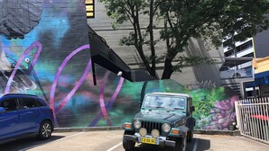 A parking area with a mural on the wall, a blue car, and a green vehicle.